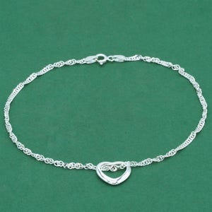 May include: A silver bracelet with a heart-shaped charm. The bracelet has a delicate chain design and a lobster clasp. The heart pendant is centrally placed, adding a touch of elegance to the piece.
