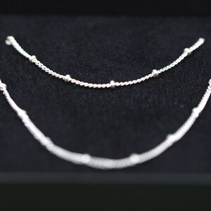 May include: Two silver necklaces with small round beads on a black background.