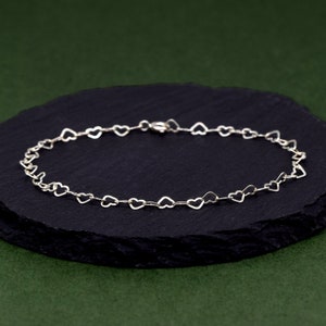 May include: A silver heart-shaped chain bracelet on a black background.