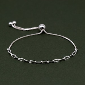 May include: A silver chain bracelet with a sliding clasp. The chain is made of small, rectangular links.