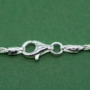 May include: Close-up of a silver chain necklace clasp with a lobster claw closure. The clasp is marked with "925" indicating sterling silver.