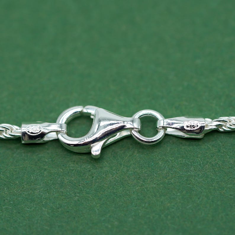 May include: Close-up of a silver chain necklace clasp with a lobster claw closure. The clasp is marked with "925" indicating sterling silver.