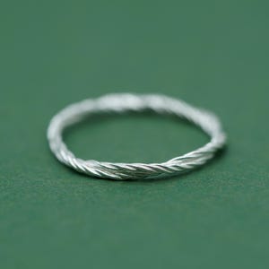 May include: A silver ring with a twisted, rope-like design. The ring is on a green background.