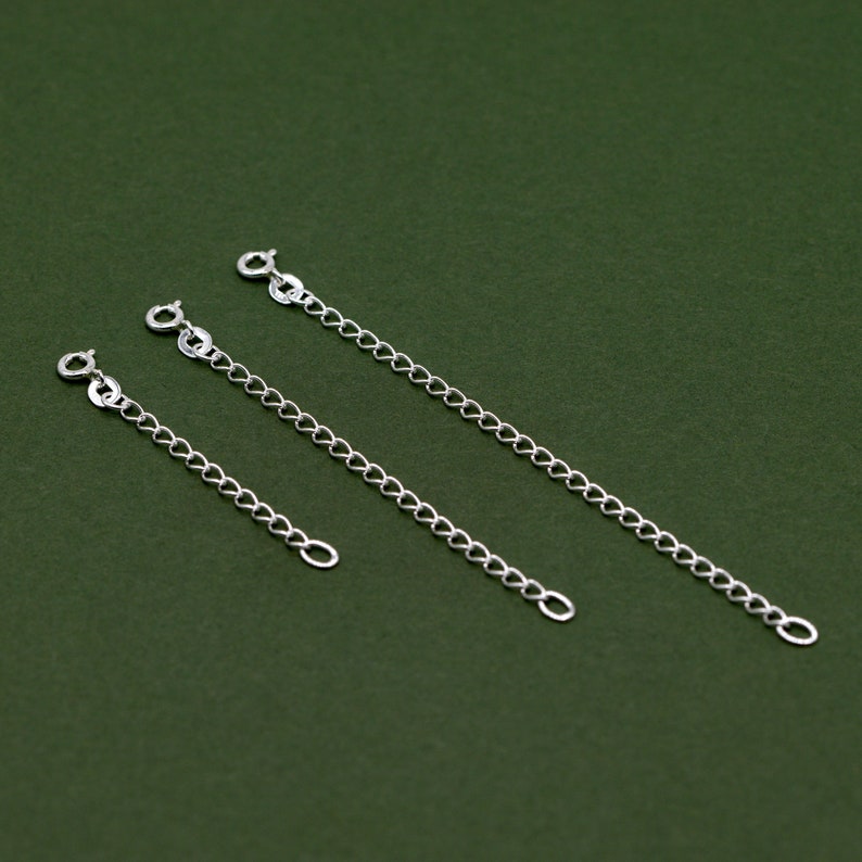 May include: Three silver chain extenders of different lengths on a green background.