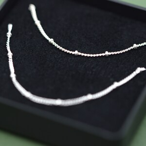 May include: Two silver necklaces with small beads on a black velvet background.