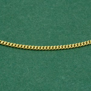 May include: A gold-colored curb chain necklace against a green background. The chain is made of interlocking, rounded links. The necklace is a jewelry item.