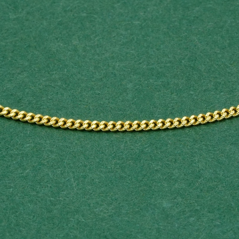 May include: A gold-colored curb chain necklace against a green background. The chain is made of interlocking, rounded links. The necklace is a jewelry item.