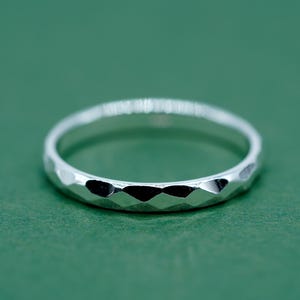 May include: A silver ring with a faceted design. The ring features a band with a series of small, geometric facets. The ring is set against a green background.