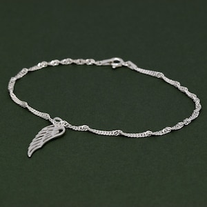 Könnte beinhalten: Ein silbernes Kettenarmband mit einem zarten Engelsflügel-Anhänger. Die Kette ist im geflochtenen Stil.