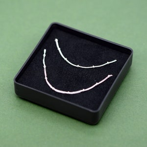 May include: Two silver necklaces with small beads, displayed in a black velvet box.