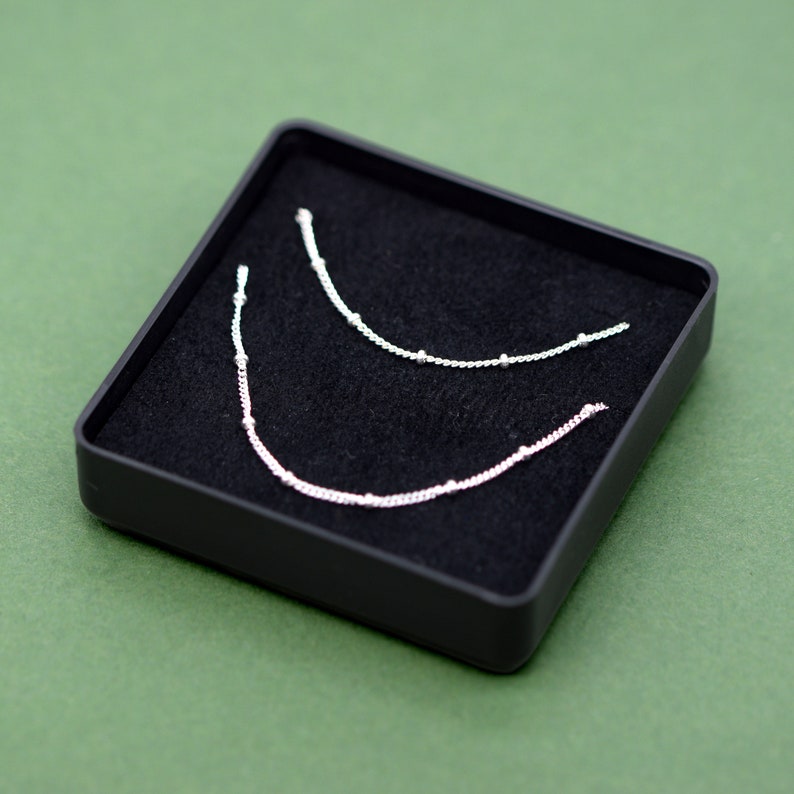 May include: Two silver necklaces with small beads, displayed in a black velvet box.