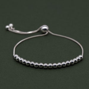 Könnte beinhalten: Ein silbernes Perlenarmband mit einem Schiebeverschluss. Das Armband besteht aus kleinen, runden Perlen und hat eine zarte Kette.