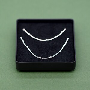 May include: Two silver necklaces with small beads on a black velvet background.