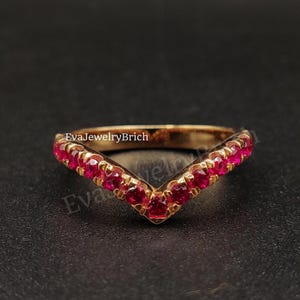 Op de afbeelding: Een gouden ring met een V-vormige rij rode edelstenen. De ring ligt op een zwarte achtergrond.