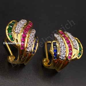 Puede incluir: Aretes de aro de oro con un diseño de piedras multicolores. Los aretes presentan una fila de piedras verdes, rosas, azules y blancas.