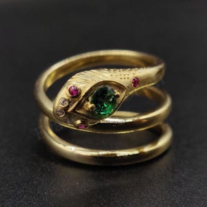 Peut inclure: Une bague en or en forme de serpent avec une pierre précieuse verte et des pierres précieuses roses. La bague est composée de trois bandes qui s'enroulent autour du doigt.