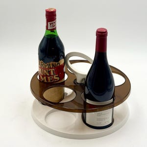 May include: A brown and white wine bottle holder with two wine bottles. The holder has a circular design with four bottle openings and a handle. One bottle has a red and white label, the other has a white label.