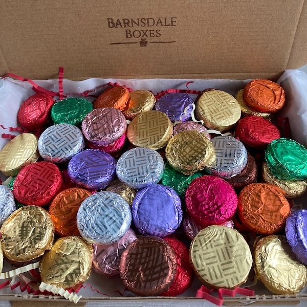 May include: A cardboard box filled with numerous foil-wrapped candies in various colors, including gold, silver, red, green, and purple. The candies are arranged inside the box with decorative paper. The box has the text "Barnsdale Boxes" printed on the inside.