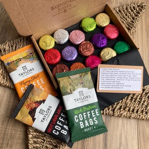 May include: A presentation box with assorted foil-wrapped chocolates and coffee bags. The chocolates are in various colours, including green, pink, and purple. Coffee bags include Flying Start, Hot Lava Java, and Rich Italian Roast 4.
