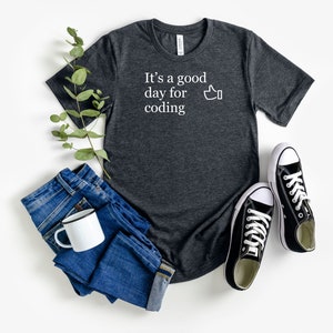 May include: A dark grey t-shirt with the text "It's a good day for coding" and a thumbs up emoji in white.