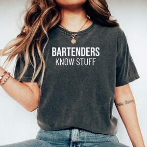 May include: A dark gray t-shirt with the text "BARTENDERS KNOW STUFF" printed in white on the front.