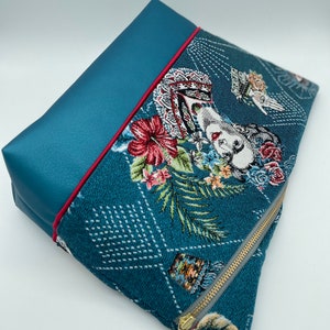 May include: A teal blue zippered pouch with a floral pattern and a gold zipper. The pouch has a teal blue flap with a red trim.