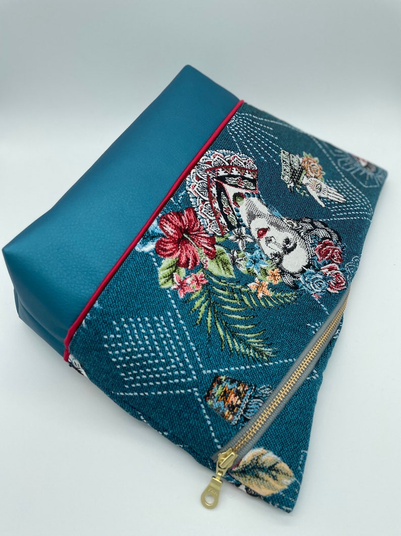 May include: A teal blue zippered pouch with a floral pattern and a gold zipper. The pouch has a teal blue flap with a red trim.
