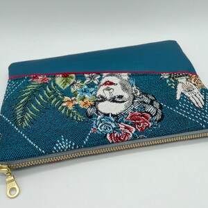 May include: A teal blue zippered pouch with a floral and geometric pattern. The pouch has a red zipper pull and a gold zipper.