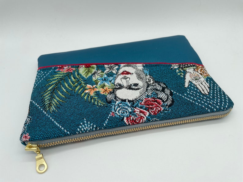May include: A teal blue zippered pouch with a floral and geometric pattern. The pouch has a red zipper pull and a gold zipper.