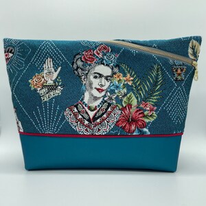 May include: A teal blue zippered pouch with a colourful tapestry design featuring a portrait of Frida Kahlo. The pouch has a red trim and a teal blue bottom.