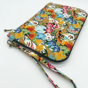 May include: A colourful floral print clutch with a wrist strap. The print features stylised faces and flowers in shades of orange, yellow, blue, green, pink and white.