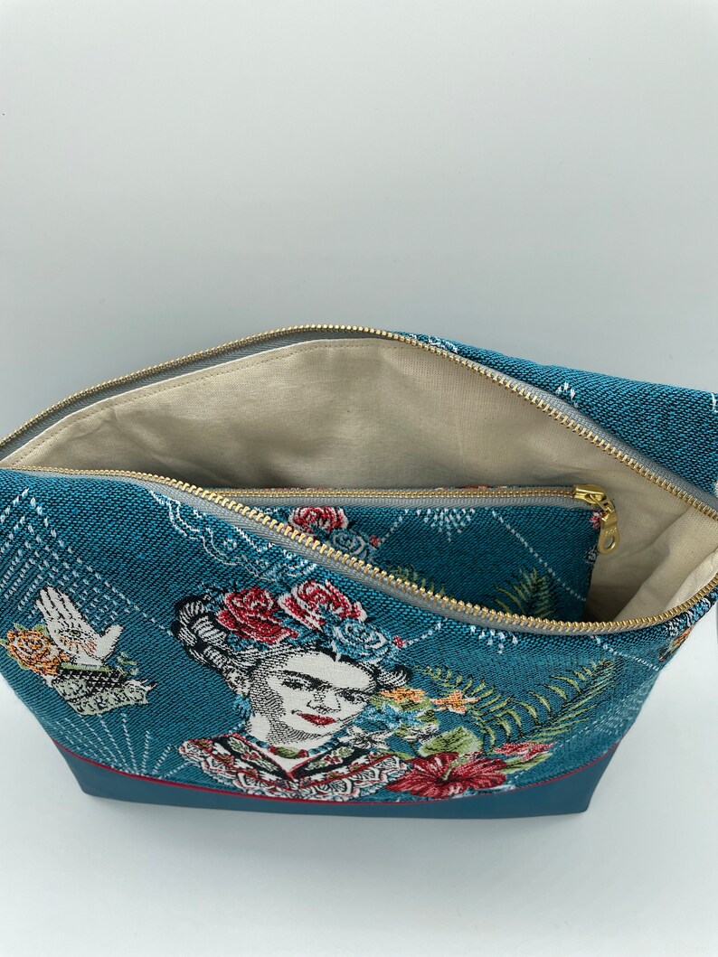 May include: A blue zippered pouch with a woven design featuring a portrait of Frida Kahlo with flowers. The pouch has a smaller zippered pocket inside.