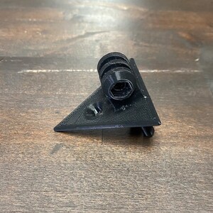 May include: A black plastic triangular camera mount with a threaded hole for attaching a camera.