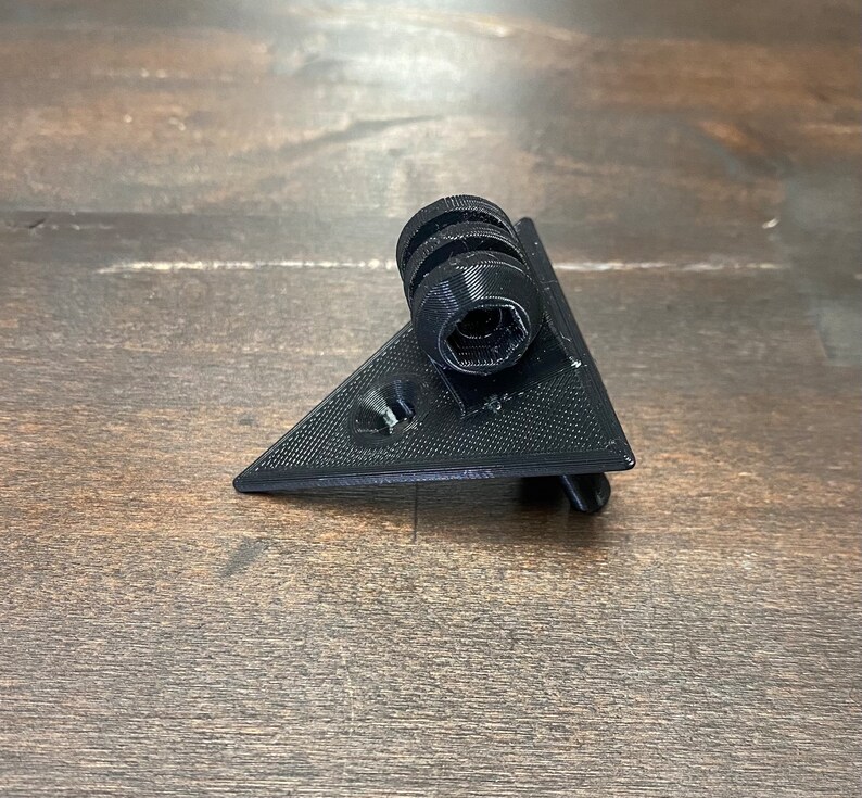 May include: A black plastic triangular camera mount with a threaded hole for attaching a camera.