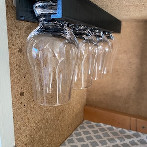 May include: Black under-cabinet glass rack with five clear glasses hanging from it.