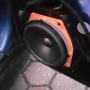 May include: A close-up of a car speaker with an orange and gray surround. The speaker is mounted in a car door.