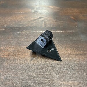 May include: A black 3D printed triangular camera mount with a hole in the center and a threaded hole on the top.
