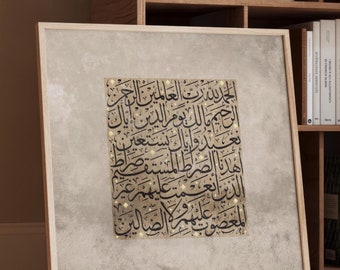 May include: A framed artwork featuring Arabic calligraphy in black script on a beige background with a textured appearance. The frame is light-colored wood. The artwork is leaning against a wooden bookshelf.