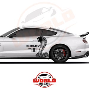 May include: White car with black Shelby GT500 graphics. The design features a cobra snake and the text "SHELBY GT500" in black. The car has black wheels with red brake calipers and a rear spoiler.