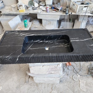 May include: A black marble countertop with a built-in rectangular sink. The countertop has white veining and a textured, grooved edge. The sink has a single faucet hole.