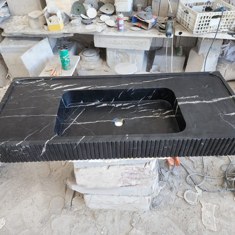 May include: A black marble countertop with a built-in rectangular sink. The countertop has white veining and a textured, grooved edge. The sink has a single faucet hole.