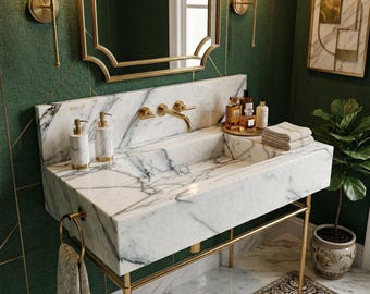May include: A luxurious bathroom sink made of white marble with gray veining. The sink has a gold faucet and is supported by a gold metal frame. Soap dispensers and towels are visible. The background features a green wall and gold accents.