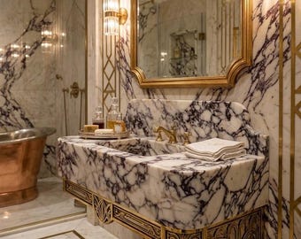 May include: A wall-mounted bathroom vanity crafted from white marble with deep purple veining, featuring ornate gold metal brackets. Above the vanity sits a gold-framed mirror flanked by two cylindrical glass wall sconces with gold accents.