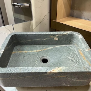 Peut inclure: &Eacute;vier rectangulaire en pierre aux coins arrondis. L'&eacute;vier est de couleur gris-vert mouchet&eacute; avec des stries de beige et de blanc. Il poss&egrave;de un seul trou d'&eacute;vacuation au centre et est con&ccedil;u pour une utilisation dans la salle de bain.