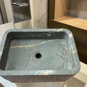 Peut inclure: Un &eacute;vier de salle de bain rectangulaire en pierre avec un motif marbr&eacute; gris fonc&eacute; et or. L'&eacute;vier a un seul trou d'&eacute;vacuation et des coins arrondis. L'&eacute;vier est en pierre naturelle.