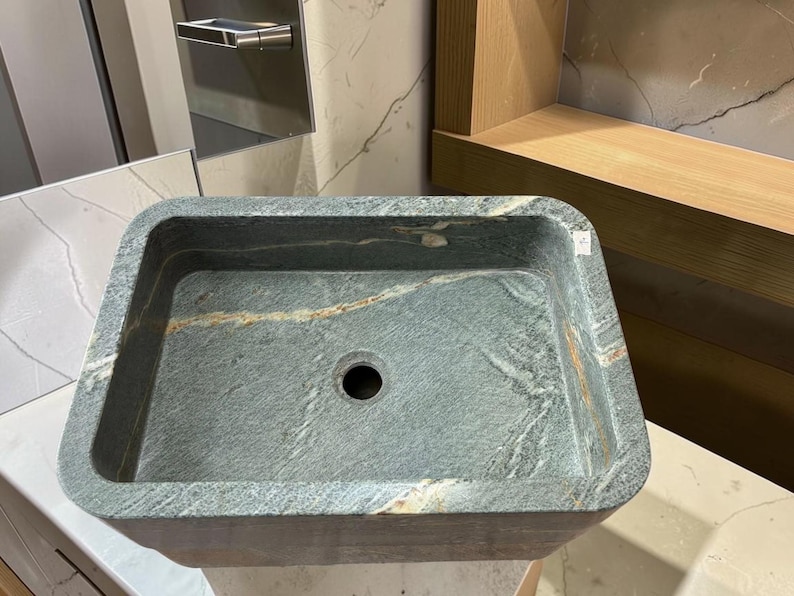 Peut inclure: Un &eacute;vier de salle de bain rectangulaire en pierre avec un motif marbr&eacute; gris fonc&eacute; et or. L'&eacute;vier a un seul trou d'&eacute;vacuation et des coins arrondis. L'&eacute;vier est en pierre naturelle.