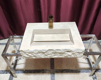 May include: A white stone sink with a rough texture and a single faucet. The sink is mounted on a metal stand with a rectangular frame.