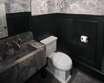 Könnte beinhalten: Ein modernes Badezimmer mit einem Marmorwaschbecken und goldenen Armaturen. Die Wände sind schwarz mit weißen Paneelen und einer Wolkenmuster-Tapete. Eine weiße Toilette befindet sich in der Ecke, und eine Toilettenpapierrolle ist an der Wand befestigt.
