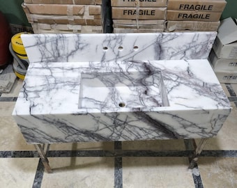 May include: White marble bathroom vanity with a purple veining pattern. The vanity has a rectangular sink and a metal stand with two legs.