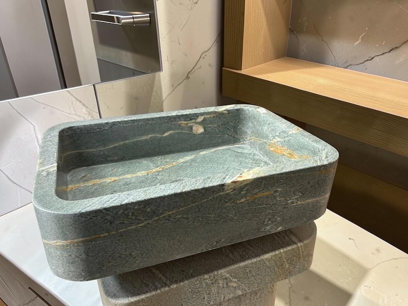Peut inclure: Un &eacute;vier rectangulaire en pierre aux coins arrondis. L'&eacute;vier est de couleur gris-vert mouchet&eacute; avec des stries de beige et d'or. L'&eacute;vier est pos&eacute; sur une surface blanche. L'&eacute;vier est de conception moderne.